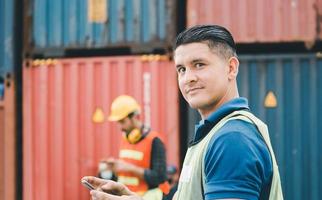 ingenieur man gebruikt mobiele telefoon, industriële werknemer met behulp van mobiele smartphone in industriële containers vracht foto