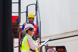 vrouwelijke voorman veiligheidsvest met behulp van klembord checklist en arbeider man in veiligheidshelm met laptop voor controle laden van containers doos van vracht foto