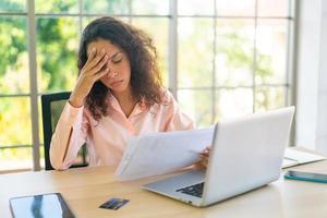 Latijnse vrouw die met laptop en papier op werkruimte werkt foto