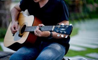 foto van een gitarist, een jonge man die gitaar speelt terwijl hij in een natuurlijke tuin zit, muziekconcept