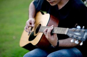 foto van een gitarist, een jonge man die gitaar speelt terwijl hij in een natuurlijke tuin zit, muziekconcept