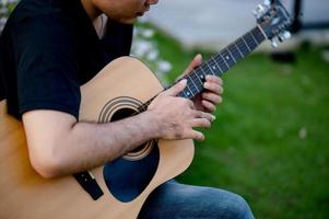 foto van een gitarist, een jonge man die gitaar speelt terwijl hij in een natuurlijke tuin zit, muziekconcept