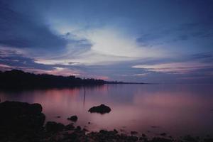 geweldig zeegezicht in een Sumatera-strand. strand met rotsen ernaast. fotografeer met een lange sluitertijd of zachte focus. weerspiegeling van bos naast het strand onder de blauwe lucht. foto