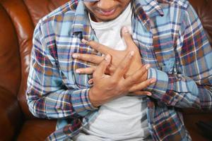 jonge man die pijn in het hart lijdt en de borst met de hand vasthoudt foto