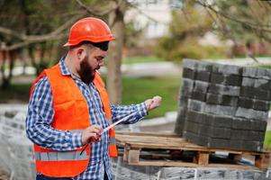 brute baard roken werknemer man pak bouwvakker in veiligheid oranje helm tegen stoep met een meetlint in de hand. foto