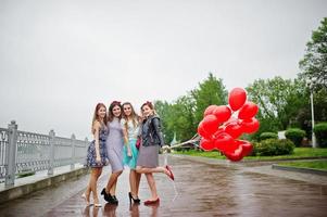 aantrekkelijke bruid poseren met haar drie mooie bruidsmeisjes met rode hartvormige ballonnen op de stoep met meer op de achtergrond. vrijgezellenfeest. foto