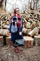 jonge hipster meisje slijtage op jas en sjaal met handtas tegen houten stronken op hout. foto