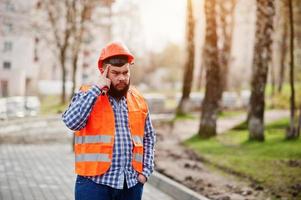 portret van brutale baard werknemer man pak bouwvakker in veiligheid oranje helm tegen stoep denken. foto