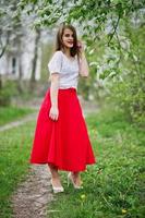 portret van mooi meisje met rode lippen in de lentebloesemtuin, draag een rode jurk en witte blouse. foto