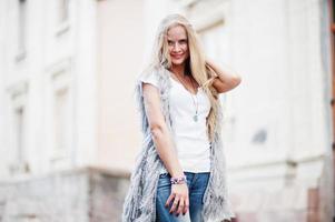 stijlvolle blonde vrouw draagt jeans en meisje mouwloos met wit overhemd tegen straat. mode stedelijk model portret. foto