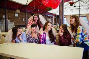groep vrolijke meisjes op geruite shirts zittend aan tafel op vrijgezellenfeest. meisje toont haar verlovingsring. foto