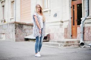 stijlvolle blonde vrouw draagt jeans en meisje mouwloos met wit overhemd tegen straat. mode stedelijk model portret. foto