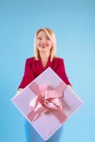 mooie lachende blonde vrouw in blazer met huidige doos in haar armen op blauwe achtergrond foto