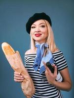 portret van mooie blonde franse vrouw in baret, sjaal, rug en wit overhemd, met fles wijn en brood stokbrood in haar armen met franse vlag op achtergrond foto