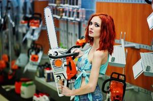 roodharig slank model poseerde met kettingzaag in de winkel of huishoudelijke winkel van werkgereedschap. foto