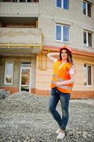 ingenieur bouwer vrouw in uniform vest en oranje beschermende helm tegen nieuwbouw. eigendom woonblok thema. foto