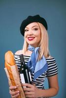 portret van mooie blonde franse vrouw in baret, sjaal, rug en wit overhemd, met fles wijn en brood stokbrood in haar armen met franse vlag op achtergrond foto