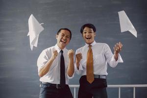 twee gelukkige aziatische zakenlieden die hun succes en prestaties vieren met vellen papier die om hen heen vliegen foto