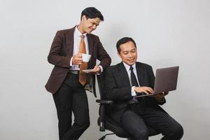 twee Aziatische zakenman in pak praten terwijl hij naar een laptop kijkt en koffie drinkt foto