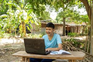 een jongen studeert met plezier online met een laptop op zijn bureau thuis op het platteland foto