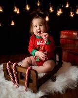 7 maanden oud meisje in een rood kerstkostuum op een achtergrond van retro slingers zit op een fur foto