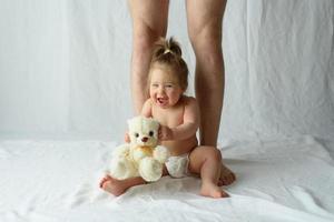 klein meisje zit gelukkig op een witte achtergrond en benen van haar vader foto