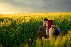 een man en een vrouw liggen op hun rug in een tarweveld. een man kust een vrouw op de wang. het meisje opende haar mond van verrukking. foto