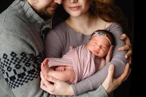 ouders houden hun pasgeboren dochter vast. foto genomen op een donkere achtergrond.