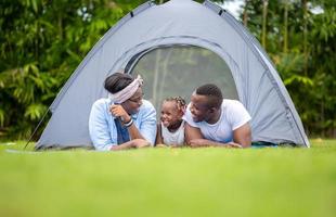 vrolijke Afro-Amerikaanse familie genieten in het park, moeder vader en dochter kamperen in de buitenlucht, geluk familieconcepten foto