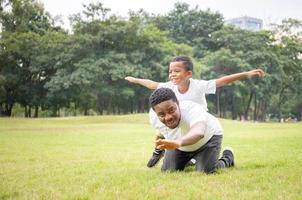 vrolijke afro-amerikaanse vader die zoon op de rug rit geeft buitenshuis glimlachen, geluk familieconcepten foto