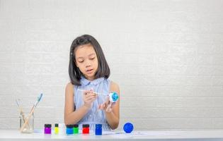 schattig klein meisje leert zonnestelsel model maken met schilderen op schuimbal foto