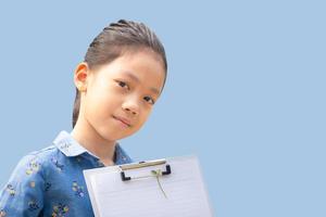 gelukkig klein schattig meisje met uitknippad klembord checklist te houden over blauwe achtergrond, onderwijs concepten. foto