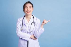 jonge aziatische vrouwelijke arts die zich op blauwe achtergrond bevindt foto