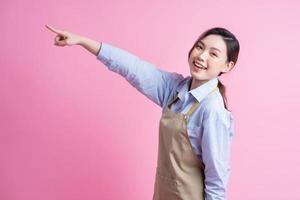 jonge Aziatische serveerster die zich op roze achtergrond bevindt foto