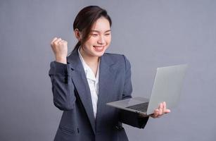 jonge aziatische zakenvrouw die een pak draagt en een laptop gebruikt op grijze achtergrond foto