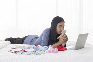 een Aziatische moeder kust de ongebruikte teddybeer van haar baby om online te verkopen in een laptop - tweedehands goed in bed. foto