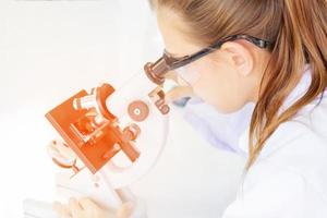 mooie vrouwelijke wetenschappers kijken naar de microscopen in een wetenschappelijk laboratorium met verschillende apparatuur in het laboratorium en hebben een oranje licht. foto