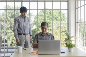 een Aziatische man van middelbare leeftijd die zijn zoon een baan leert die naast een bureau in een kantoor staat. foto