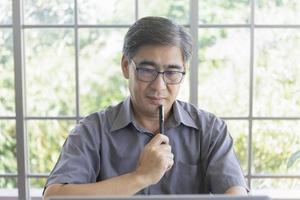 een oudere Aziatische man die een denkend gebaar maakt in zijn hand met een pen