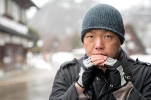 de aziatische man met sneeuwhoed staart in de camera en denkt iets, shirakawako-vallei op de achtergrond van het sneeuwseizoen. foto