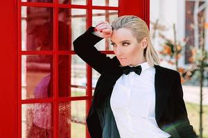 portret van stijlvolle mooie blonde vrouw in man zwart pak in de buurt van rode telefooncel foto
