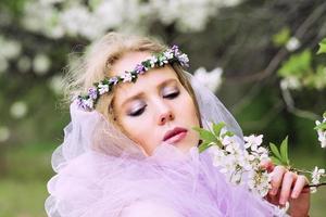 mooie jonge blonde vrouw in bloemenkrans bloeiende bomen in de lente foto