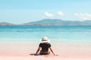 vrouw met zomerhoed die van de zomervakantie geniet en op het roze zandstrand van labuan bajo . zit foto