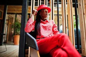 mooie vlechten zakelijke afro-amerikaanse dame heldere bazige persoon vriendelijke slijtage kantoor rood shirt, hoed en broek. foto