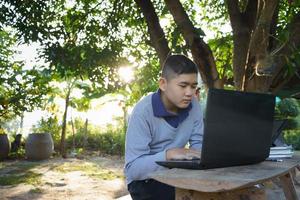 jongen studeert online op een houten tafel met een laptop en tablet tijdens de ochtenduren in een landelijk huis. concept online onderwijs platteland en thuiswerken foto