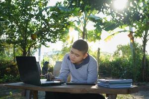 jongen studeert online op een houten tafel met een laptop en tablet tijdens de ochtenduren in een landelijk huis. concept online onderwijs platteland en thuiswerken foto