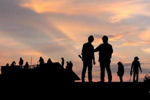 silhouet van ingenieur en werknemer op bouwplaats, bouwplaats bij zonsondergang in de avondtijd foto