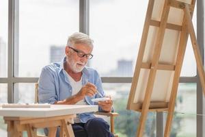 senior man schilderen op canvas thuis, oudere man schilderen op een canvas, gelukkige pensionering concepten foto