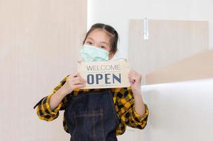 Aziatisch meisje met een schort blij gezicht glimlachend met open bord houten bord kijkend naar de camera foto
