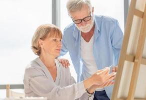 portret van gelukkig senior paar schilderen op een doek in de woonkamer, oudere man en vrouw tekenen samen op een doek, gelukkige pensionering concepten foto